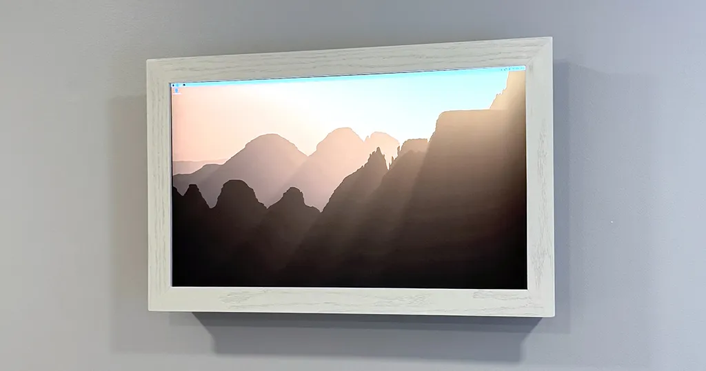 The finished 4K digital picture frame in its white wooden surround, hanging on a grey wall