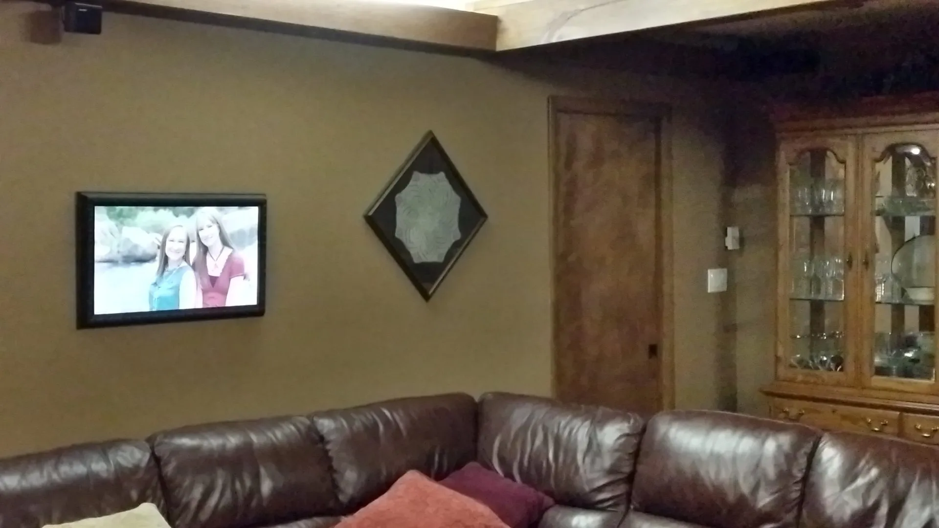A large digital frame in a dark ornate wooden frame on a basement wall, showing a photo of two young women by a river