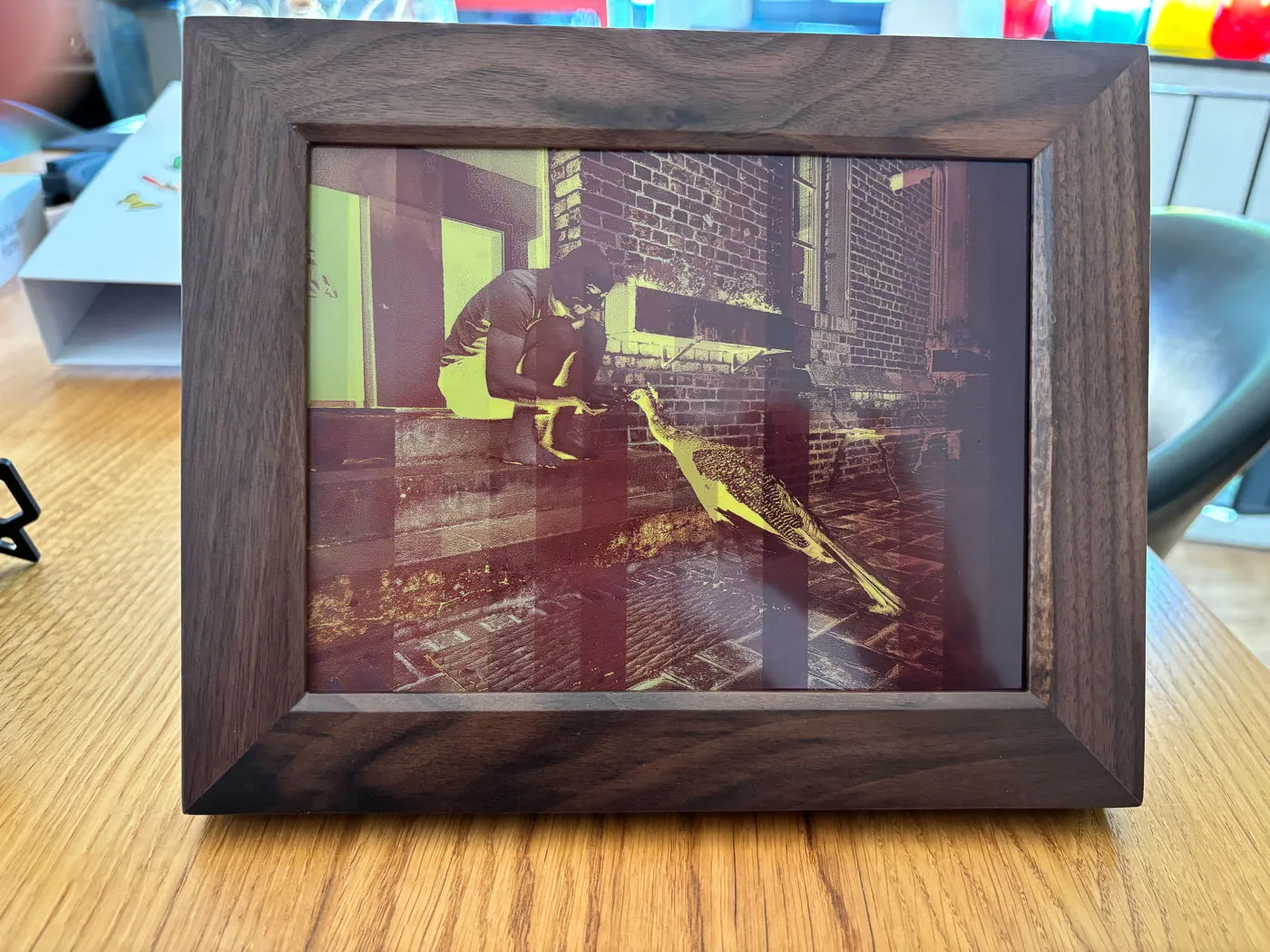 The walnut Reflection Frame halfway through a picture change, with the image in red and yellow