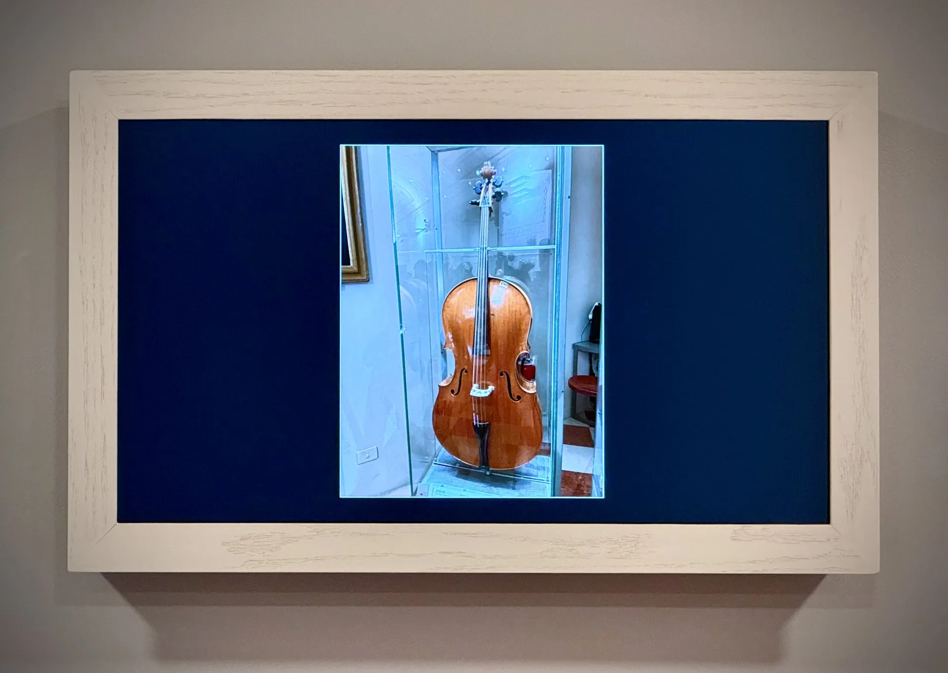A 4K digital photo frame in a simple wooden surround on a wall, showing a matted photograph